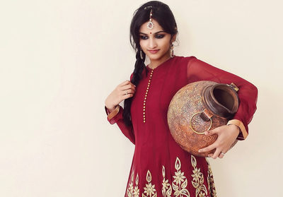A graceful woman in a red embroidered Indian outfit carries a traditional clay pot, capturing cultural heritage and timeless beauty. Her poised expression and intricate attire highlight tradition, elegance, and the artistry of rural craftsmanship.
